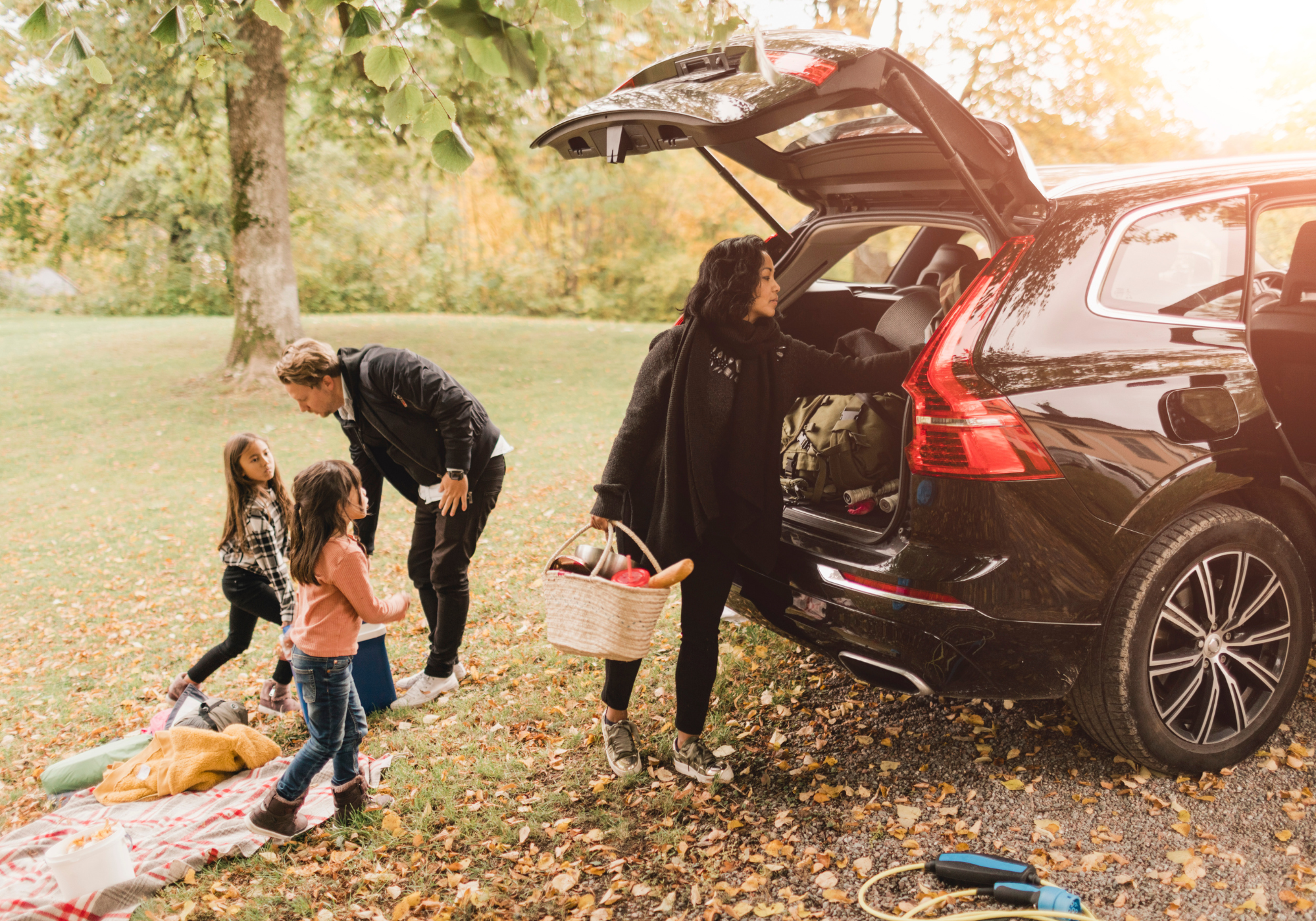 Happy family sitting in the open trunk of an SUV parked at the beach, smiling and enjoying the sunny day together.
